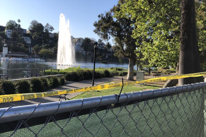A green fence surrounds Echo Park Lake, with the lake's fountain visible in the distance.