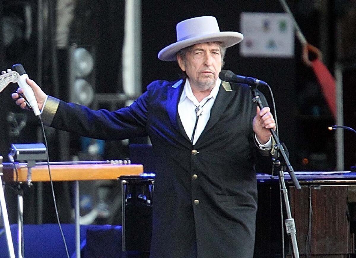 Bob Dylan, in gaucho hat and bolo tie, stands on stage behind a microphone.