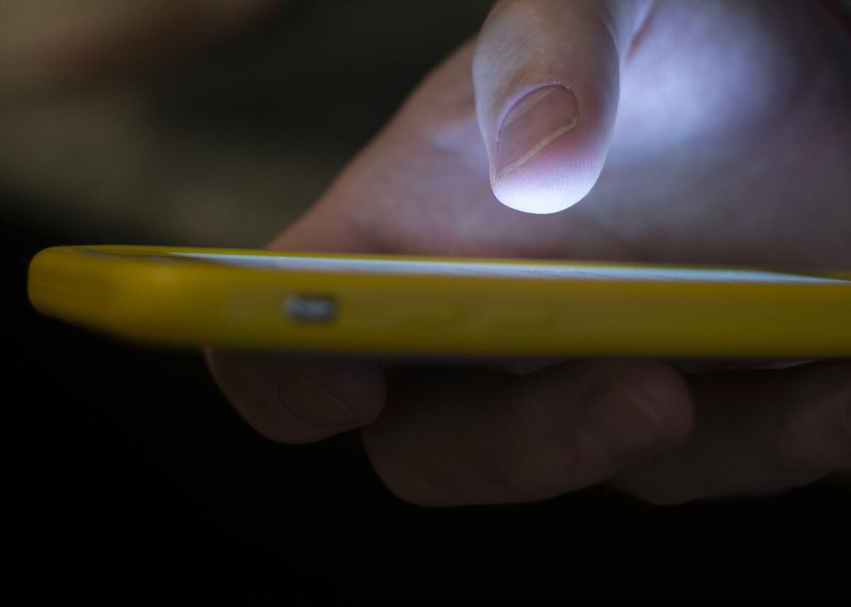 Close up of hand holding a yellow cellphone with screen glowing