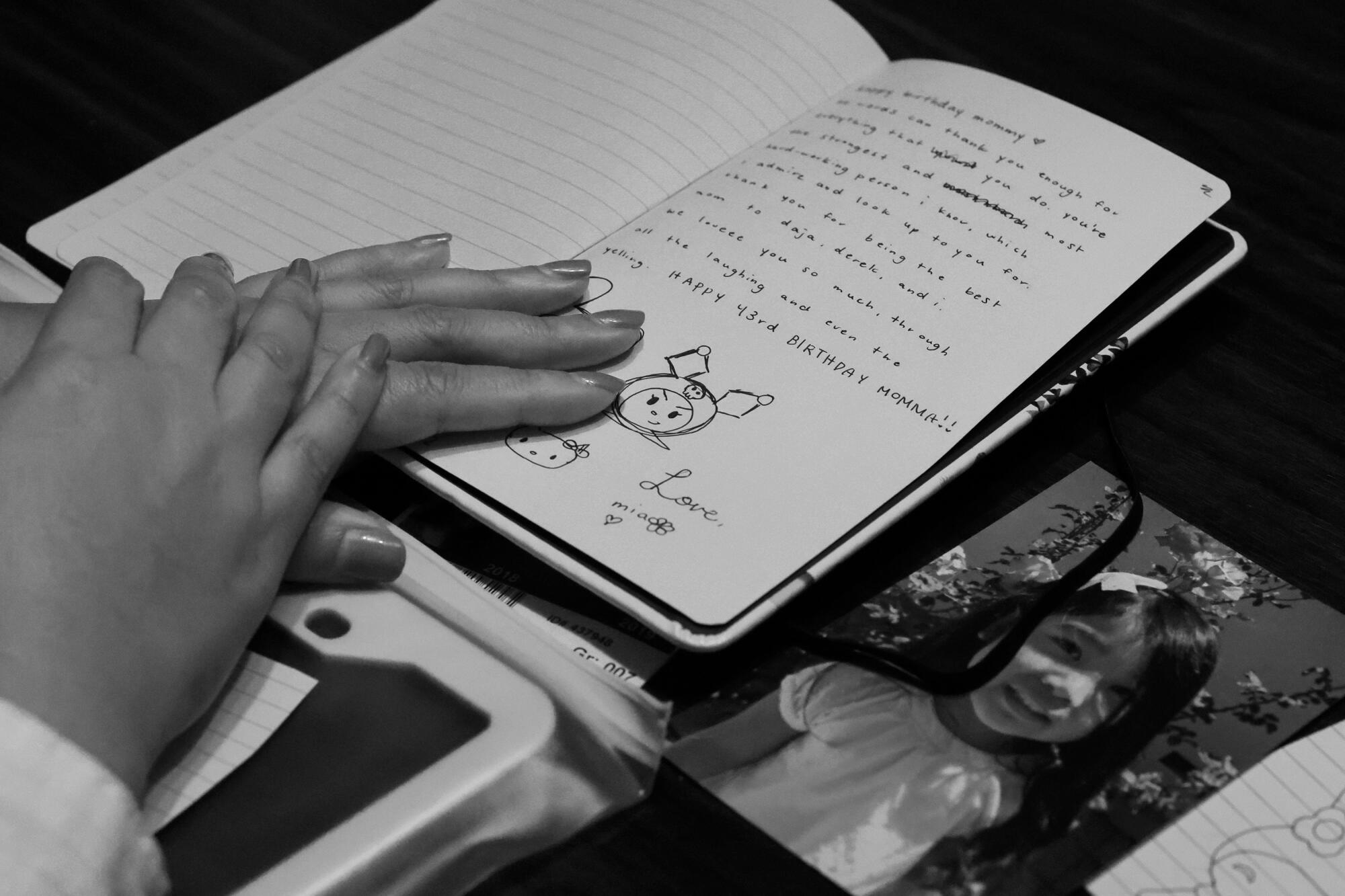 A pair of hands lie on a journal on top of a photo of a girl.