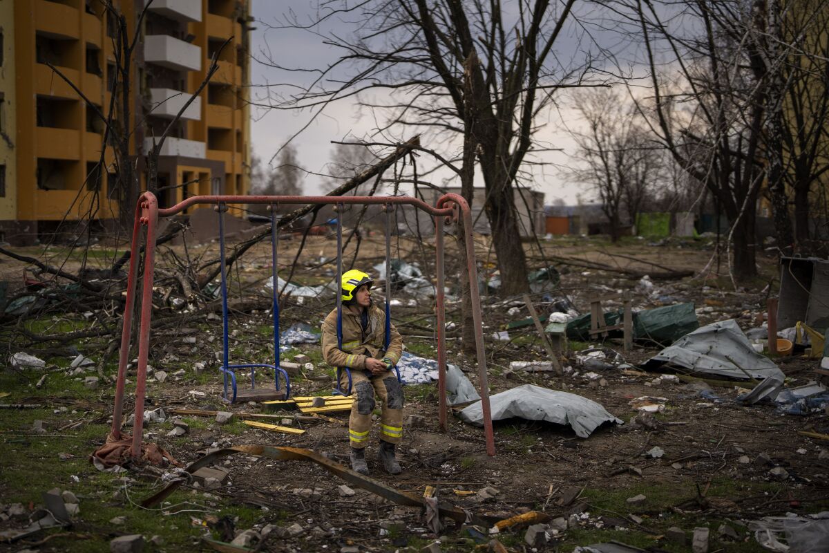 A firefighter sits on a swing next to a damaged building. 