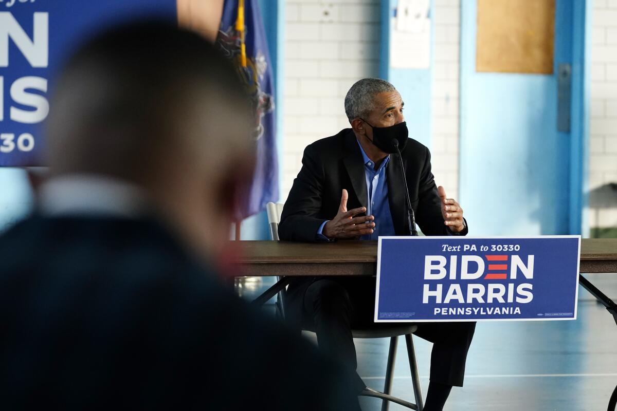 Former President Obama sits at a table with a Biden-Harris Pennsylvania campaign sign