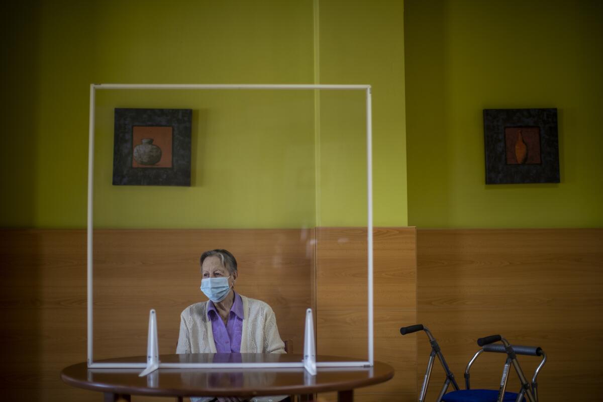 A resident awaits the visit of her family behind glass meant to protect against COVID-19 at DomusVi nursing home in Leganes, Spain, Wednesday, March 10, 2021. Spain is preparing to tighten some pandemic restrictions on movement during the approaching Easter holiday, which is a traditional period for family visits. (AP Photo/Manu Fernandez)