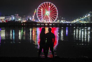 Samantha Sloss and Antonio Robles stand at the edge of the San Dieguito River as they watch the lights of the San Diego County Fair on Wednesday, June 12, 2019 in Del Mar, California.