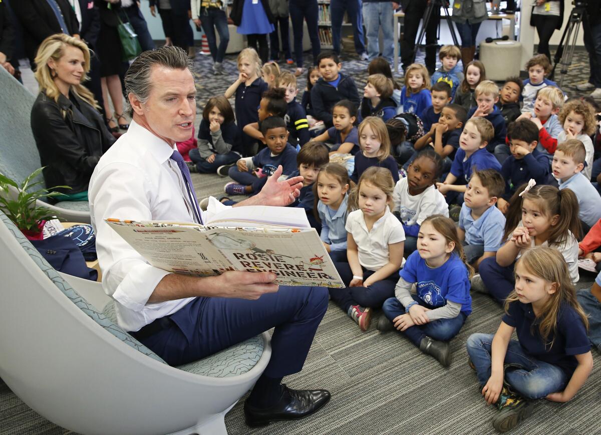 Gov. Gavin Newsom reads the book "Rosie Revere, Engineer by Andrea Beaty and David Roberts to kindergarteners at the Washington Elementary School in Sacramento, Calif., Friday, March 1, 2019. Newsom, accompanied by his wife, Jennifer Siebel Newsom, left, visited the school to celebrate Read Across America Day. (AP Photo/Rich Pedroncelli)