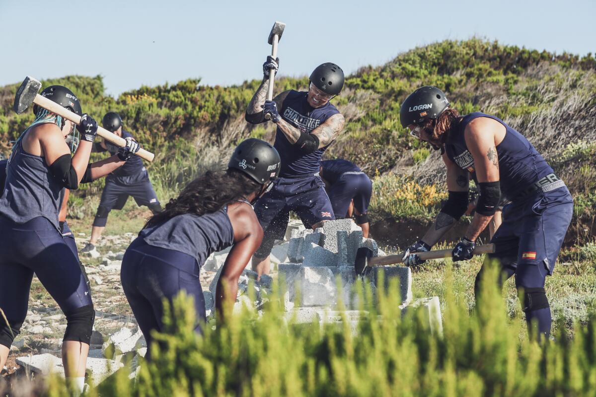 Players outdoors, wearing helmets, take sledgehammers to cinderblocks