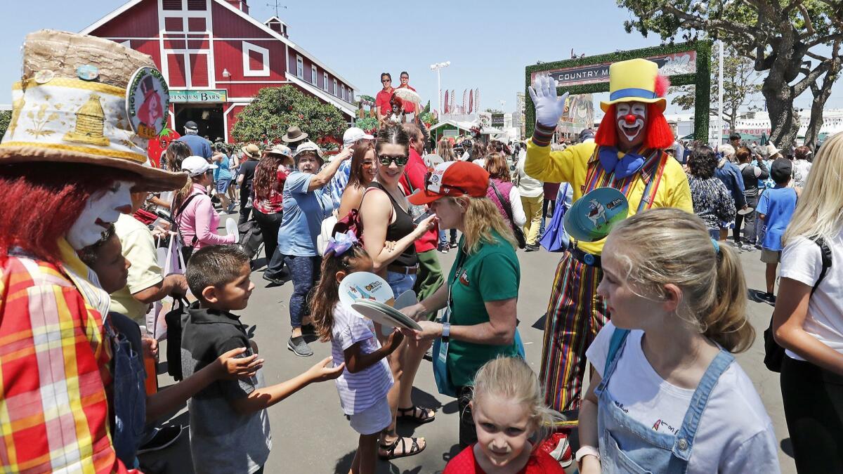 Fair clown Tadpole, right, greets visitors at the blue gate entrance on opening day for the Orange County Fair in Costa Mesa.