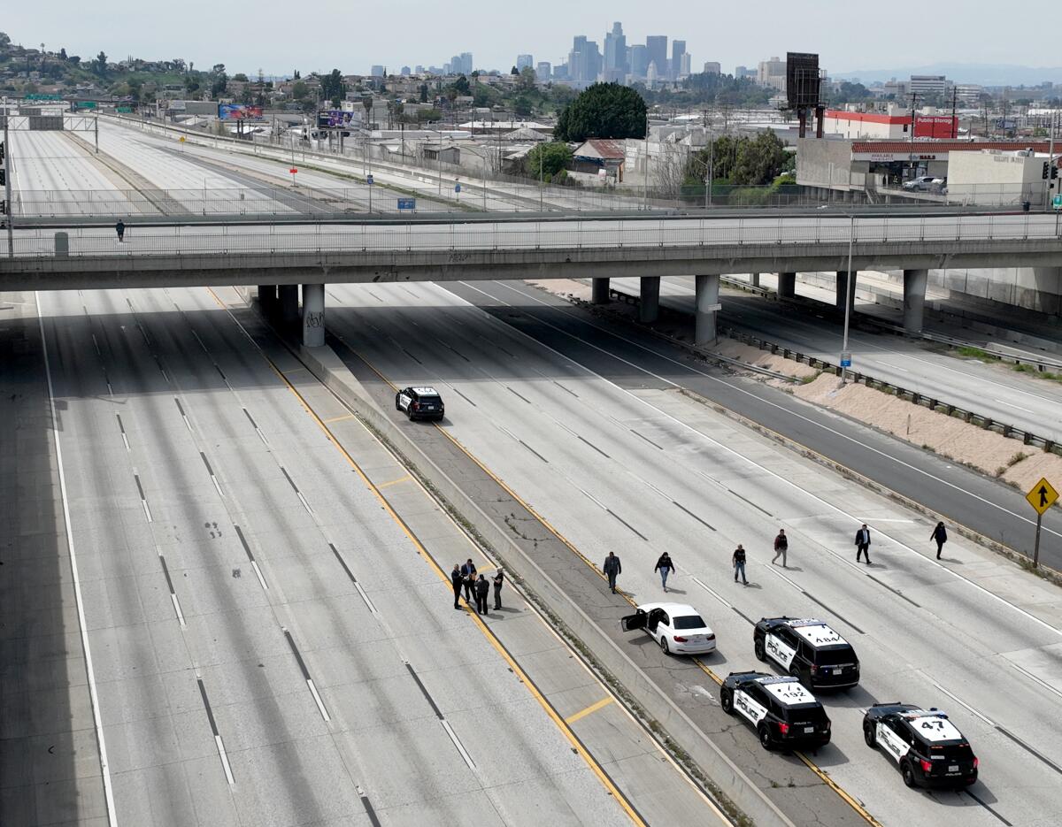 Police cruisers sit on the 10 Freeway as investigators walk down five lanes.