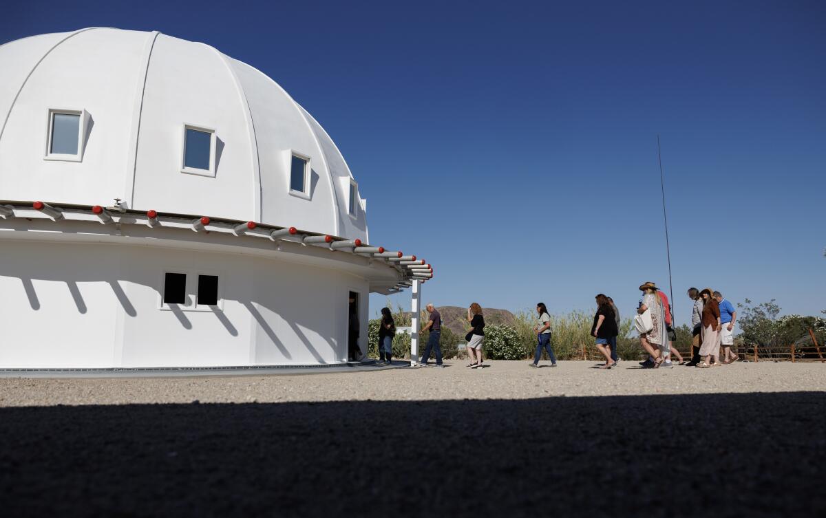 A line of people (they're from a UFO convention) walk toward the entrance of the white, domed Integratron.