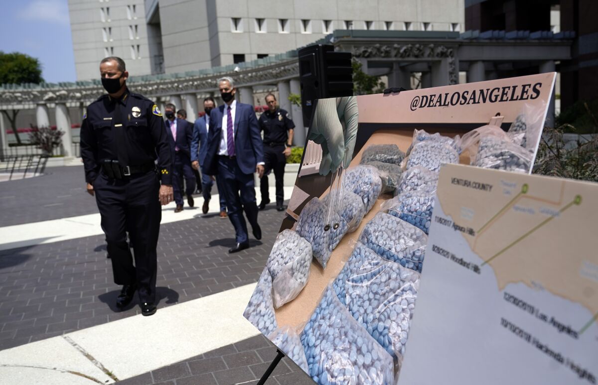 FILE - Officials walk past images of illegal drugs outside the Edward R. Roybal Federal Building, May 13, 2021, in Los Angeles. Los Angeles police say three men were found dead of suspected drug overdoses involving fentanyl. On Wednesday, May 4, 2022, officers found the dead men inside an apartment after police received a call about three unresponsive men late Wednesday. CBSLA-TV reported that a powdery drug believed to be fentanyl was found in the apartment, along with drug paraphernalia. (AP Photo/Marcio Jose Sanchez, File)