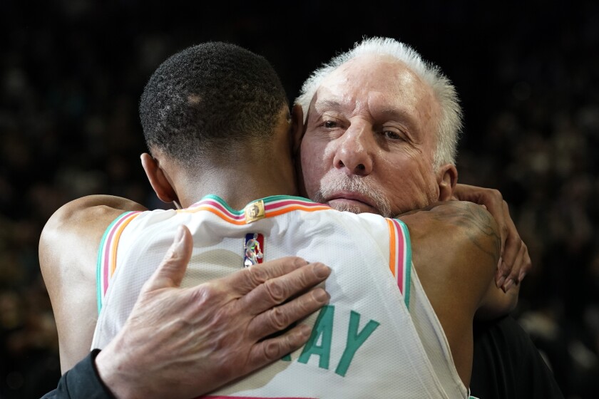 San Antonio Spurs coach Gregg Popovich, right, is hugged by guard Dejounte Murray the team's NBA basketball game against the Utah Jazz, Friday, March 11, 2022, in San Antonio. San Antonio won, making Popovich the winningest coach in NBA regular-season history. (AP Photo/Eric Gay)