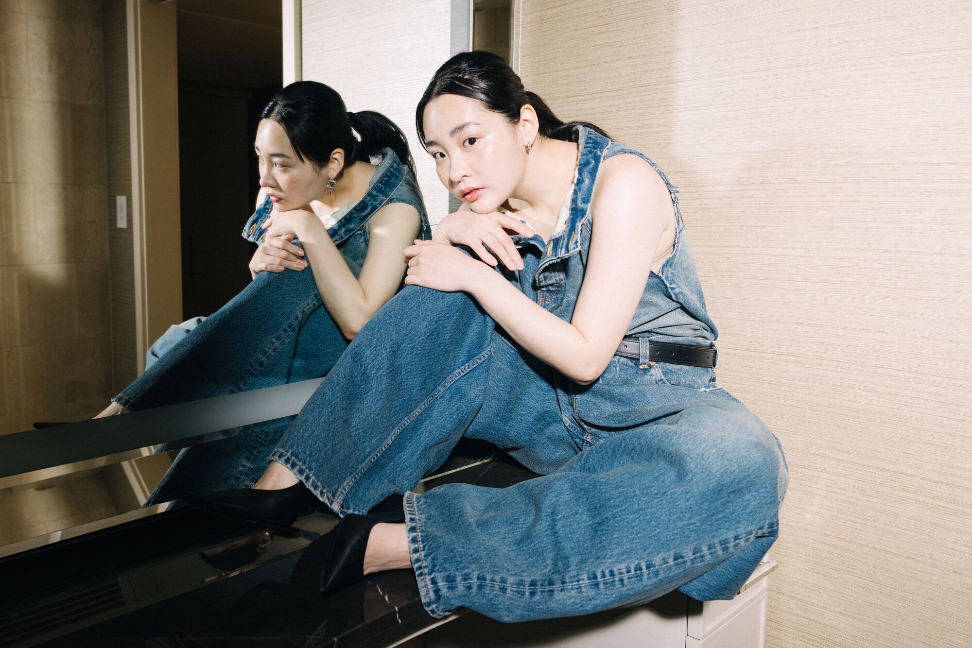 A woman in faded denim poses atop a bathroom vanity.