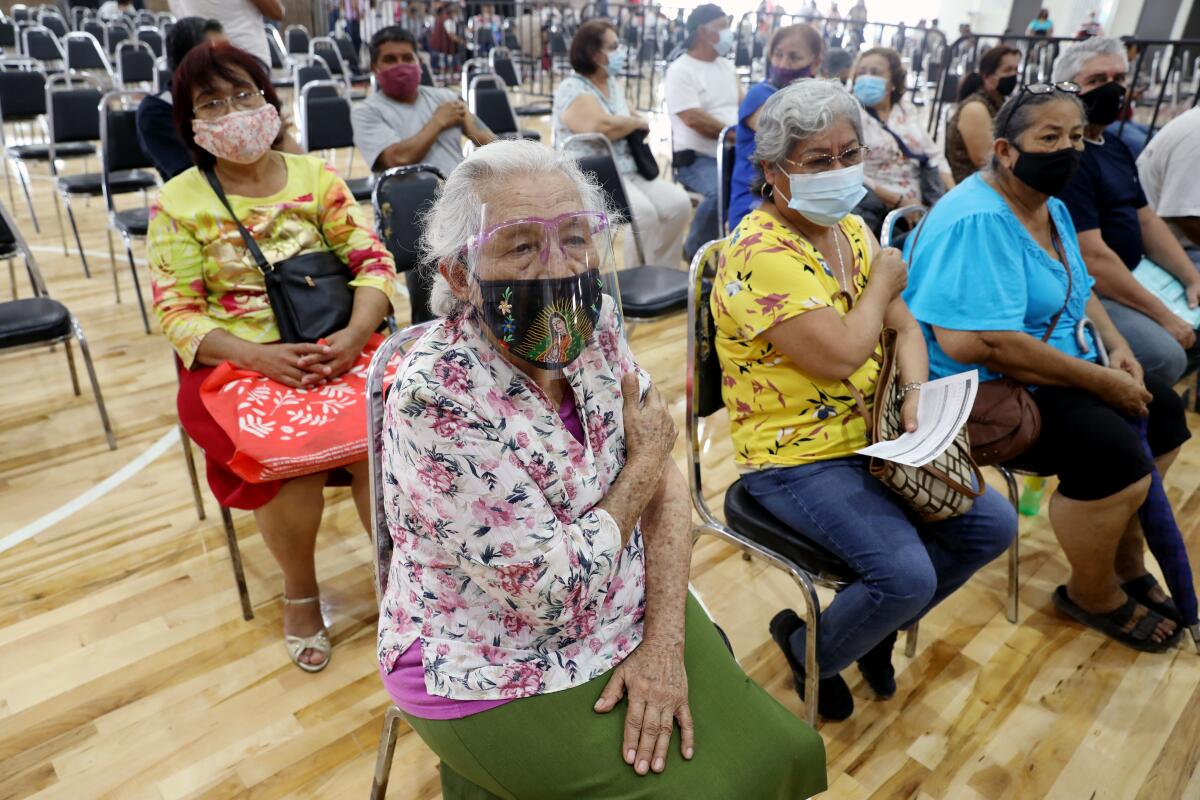 Two masked women put pressure on their arm as they sit with other people after getting the Sinovac COVID-19 vaccine