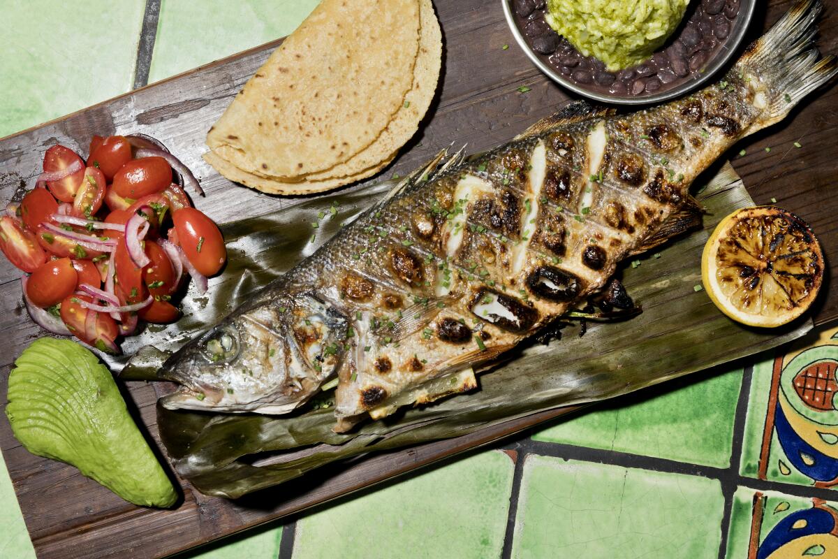 A whole grilled fish with tortillas, tomatoes and other sides