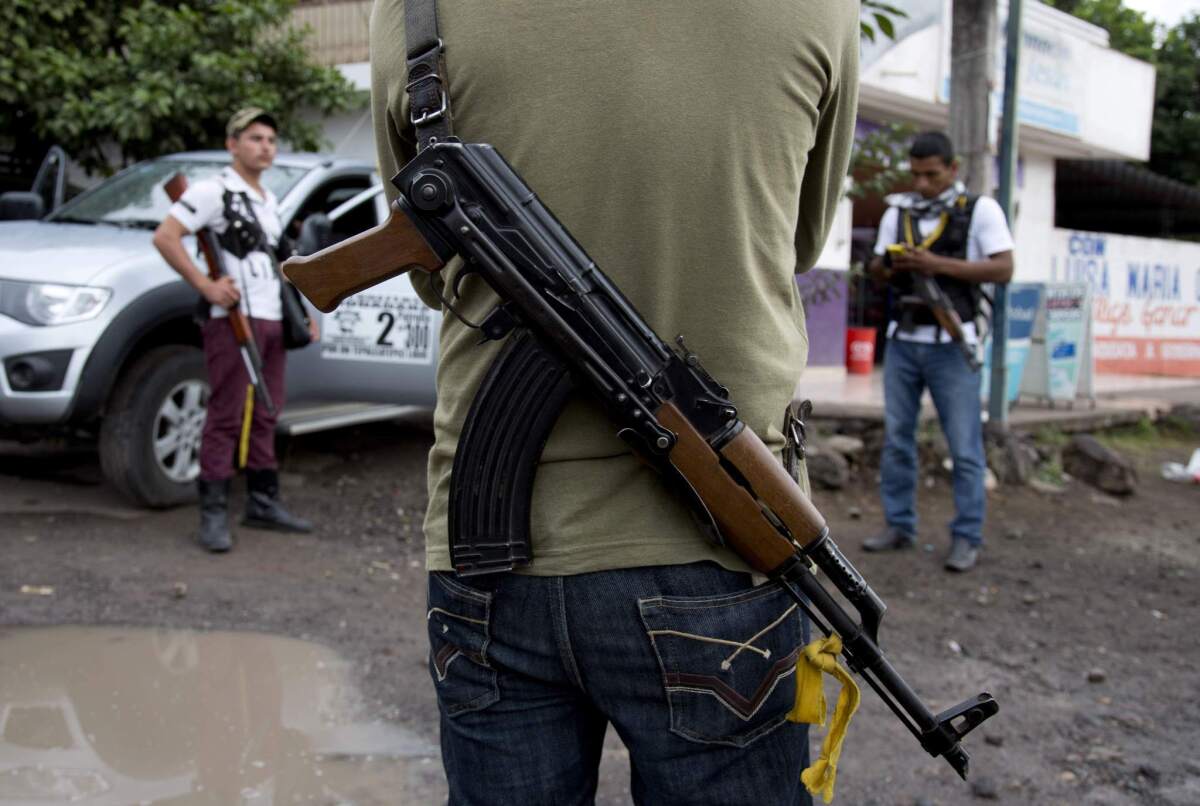 Armed men belonging to the Self-Defense Council of Michoacan stand guard at a checkpoint near the entrance to the town of Antunez, Mexico. The federal government on Tuesday announced billions in aid to the troubled state of Michoacán in the wake of clashes between armed vigilantes and a drug cartel.