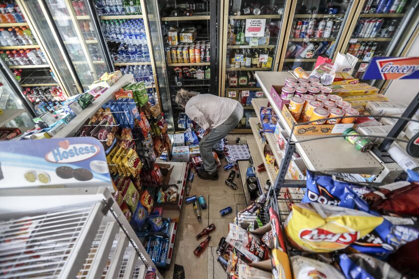 A customer rummages for a six-pack of beer at a damaged Shell food mart in Trona the day after a 7.1 earthquake.
