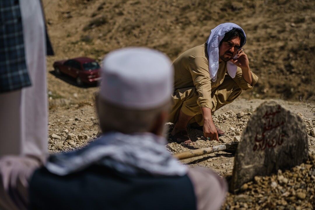 A man kneels by a grave during a funeral.