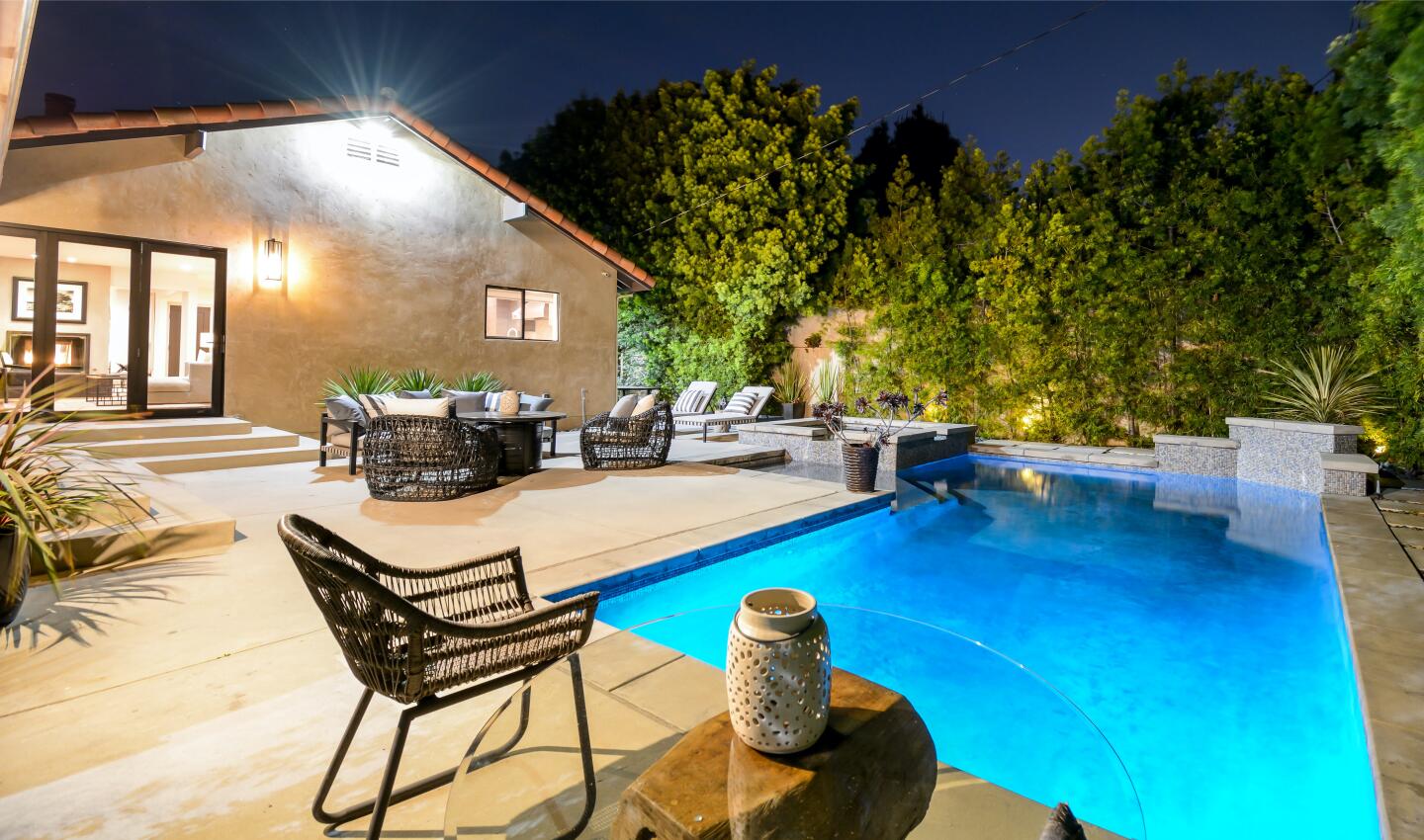 The backyard at night with a pool and patio furniture.