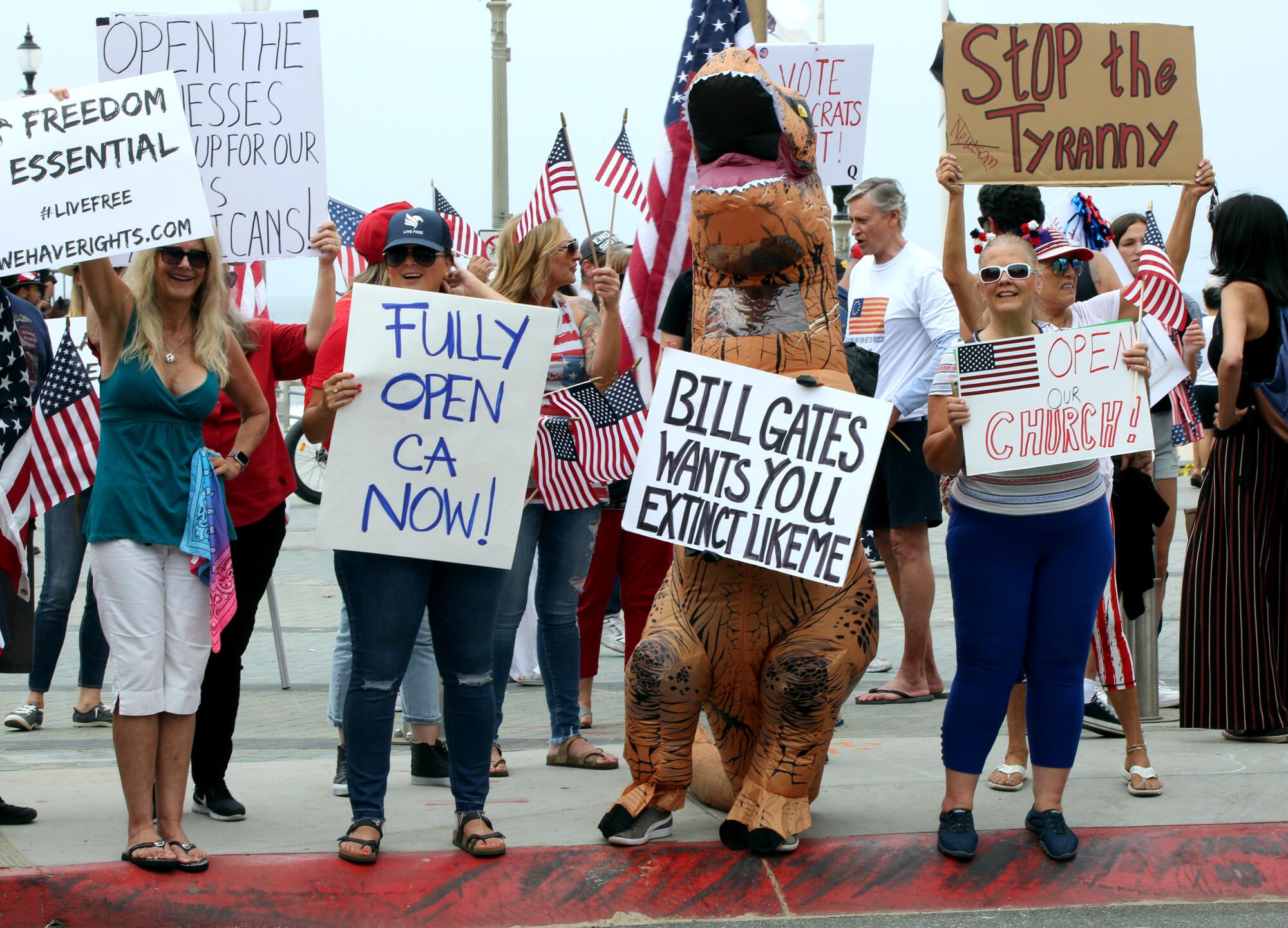 Protesters hold signs with various messages during Saturday's protest to open the state of California at Pier Plaza in Huntington Beach.