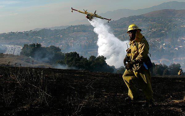 A fixed wing Super Scooper drops a load of water on smoldering brush as a Los Angeles County firefighter monitors hotspots below Scenic Ridge Drive in Chino Hills, just about the 60 freeway. A series of brush fires broke out along the 60 and 71 freeways in the Diamond Bar area.