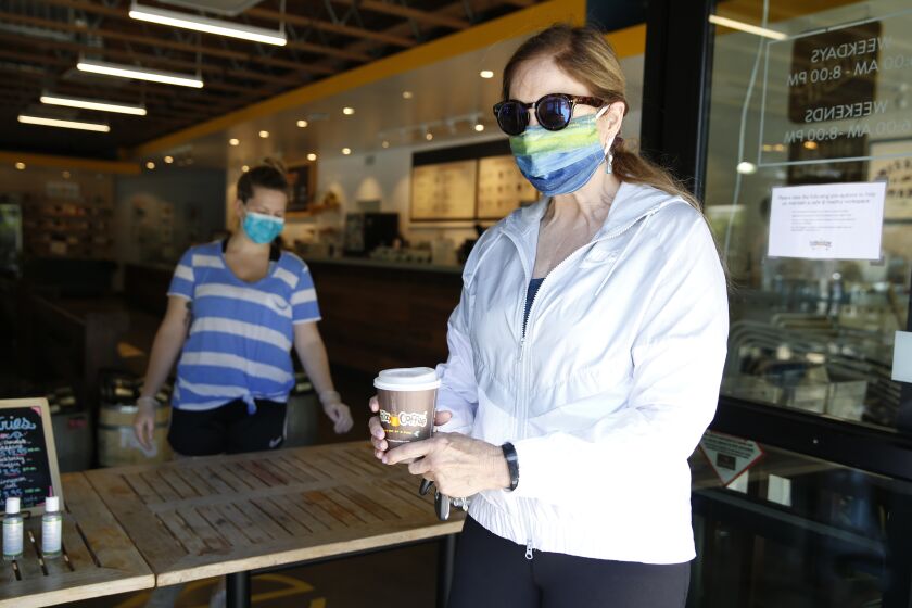Barbara Meier, right, wears a face mask as picks up her drink order from Philz Coffee in Davis, Calif., Monday, April 27, 2020. Yolo County, where Davis is located, now requires people to wear face masks in public. Face coverings are not required at home, alone in a car, outdoors, walking, hiking bicycling or running. (AP Photo/Rich Pedroncelli)