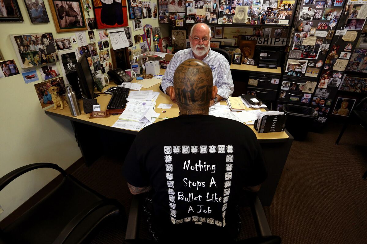Father Greg Boyle meets with Johnny Chavez, who wears a T-shirt with one of Homeboy Industries' mottos, in his Los Angeles headquarters.