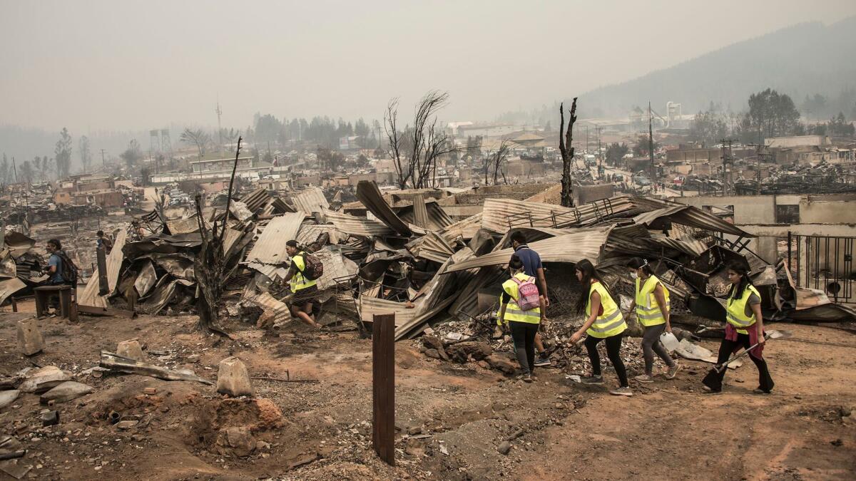 An emergency team walks through the remains of Santa Olga, Chile, about 200 miles south of Santiago, after the area was devastated by a wildfire.