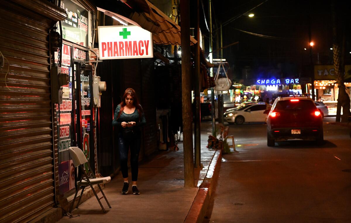 A person walks under a "Pharmacy" sign on a sidewalk.