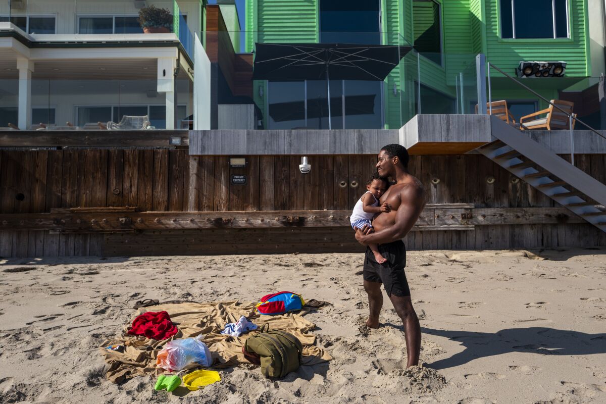 A man holds his infant son at the beach