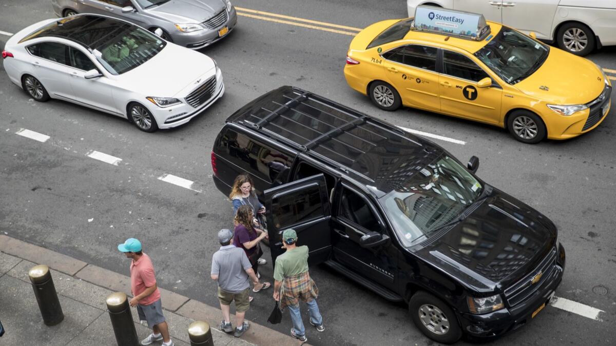 Cars in Manhattan, including a yellow taxi, make their way around a ride-hailing vehicle picking up passengers.