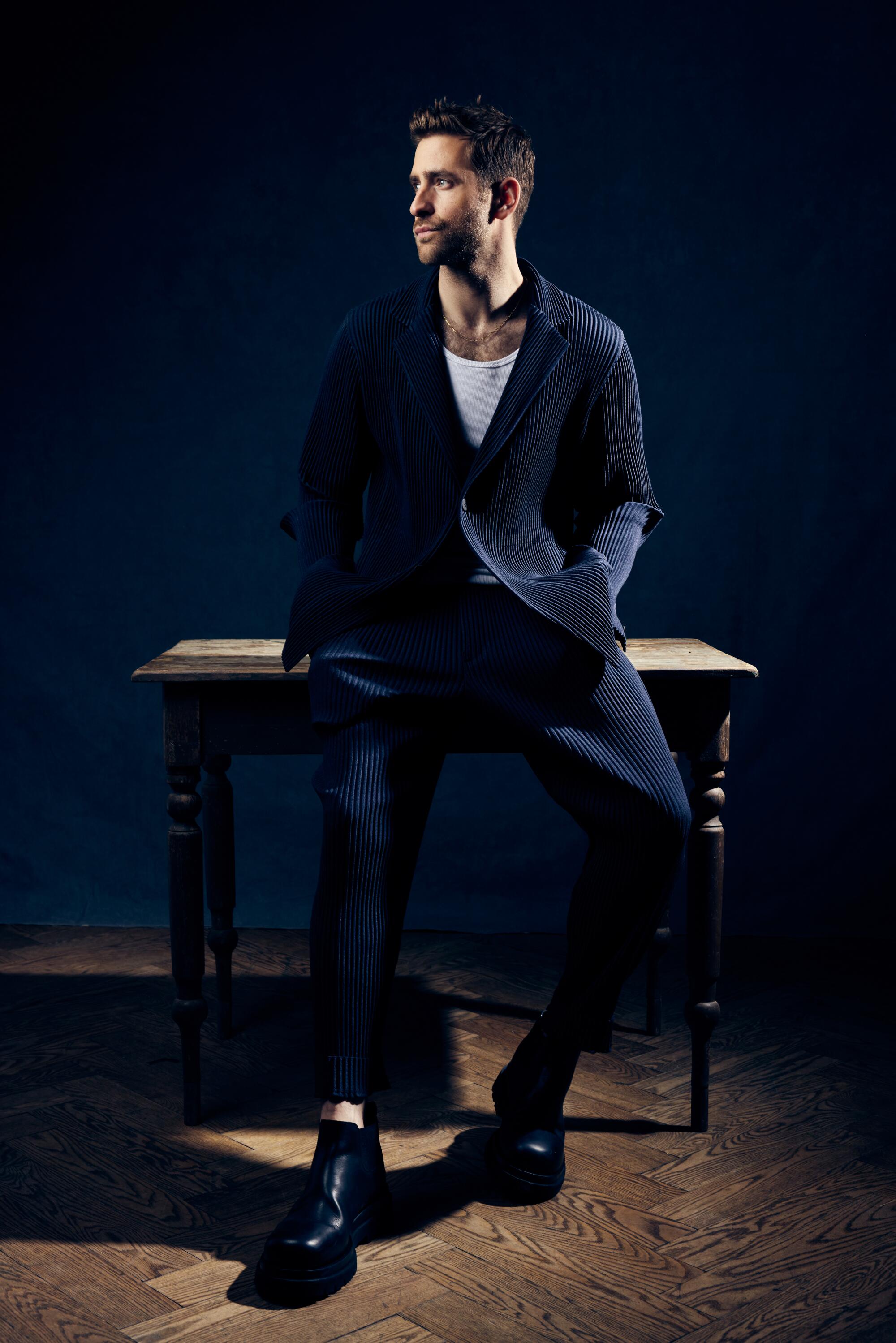 A man leans against a table and looks to the side.