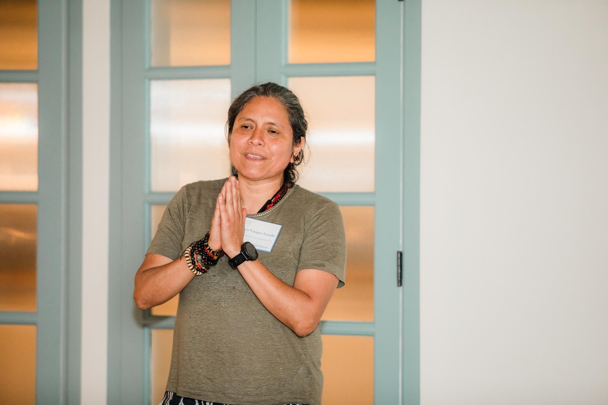 A woman stands with her hands together in a prayer position.