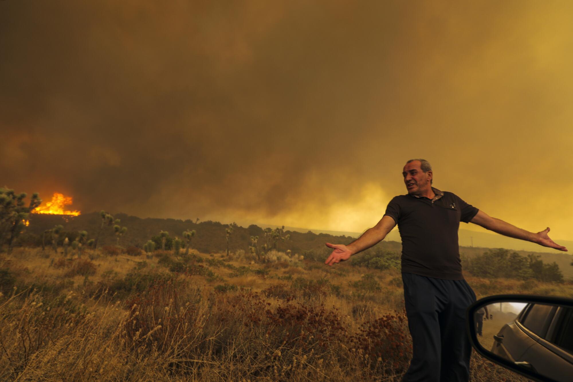 Cruthers Creek resident Mike Gregoryan stands before a hillside with flames in the distance.