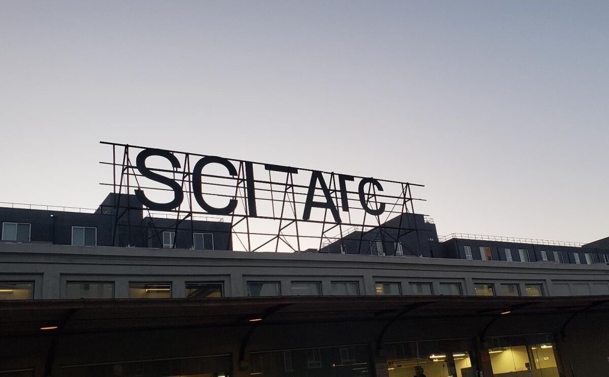 A black metal sign with SCI-Arc's name is silhouetted against a dusky sky.