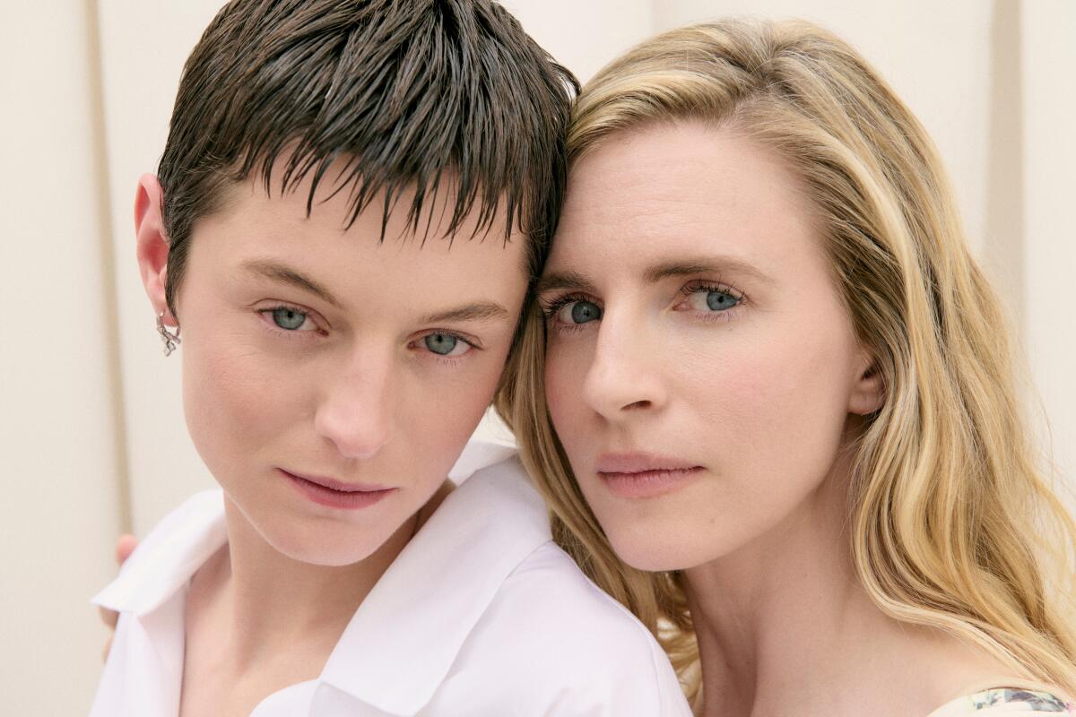 Emma Corrin and Brit Marling pose with their heads touching.