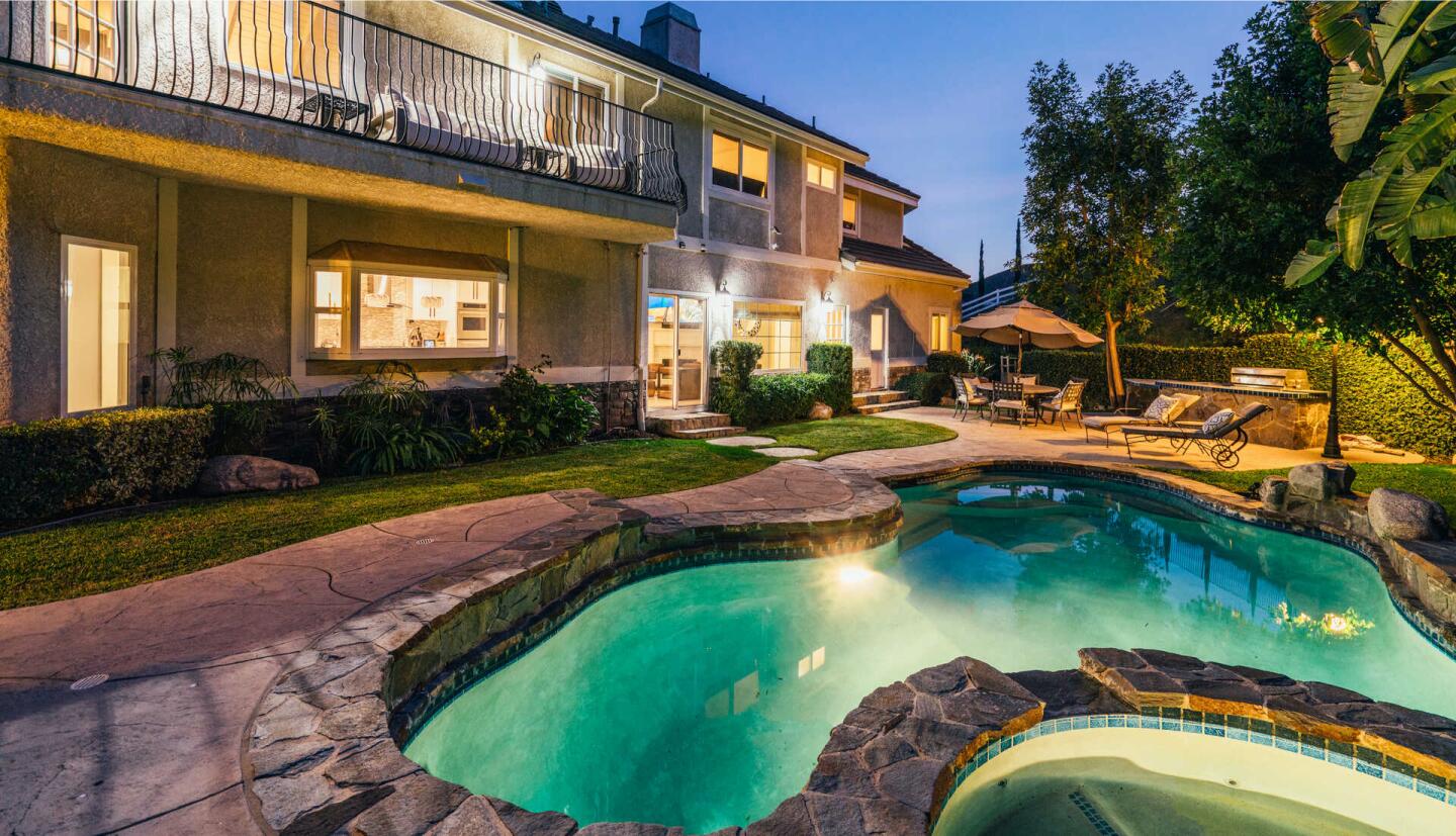 The back of the house, with seating on a second story balcony, pool and spa, at night.