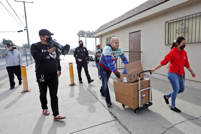 While helping load frozen turkeys onto a vehicle, Huntington Beach mayor pro temp Tito Ortiz, former UFC fighter, center, was repeatedly asked by local activist Victor Valladares, second from left with megaphone, why he wasn't wearing a mask during a Kiwanis of Huntington Beach food giveaway in the Oak View neighborhood of Huntington Beach on Wednesday, Dec. 23, 2020.