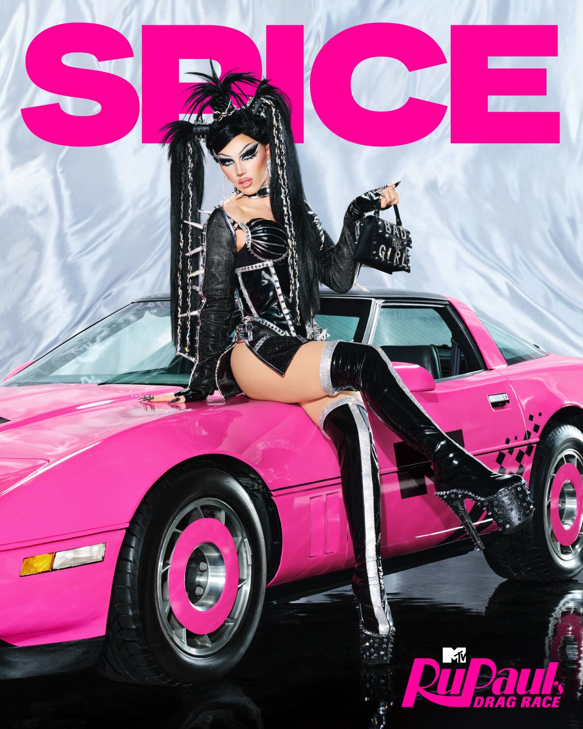 A woman in a black outfit sits on a hot pink car holding a purse up in one hand