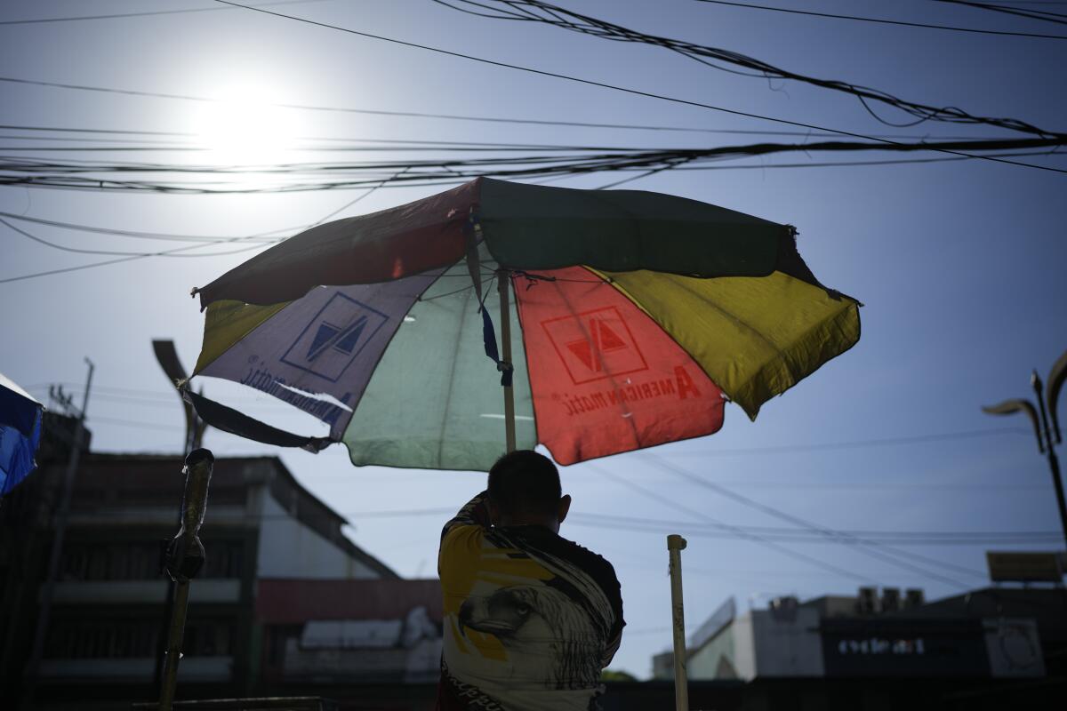 A street vendor sets up a colorful umbrella under a scorching sun. 