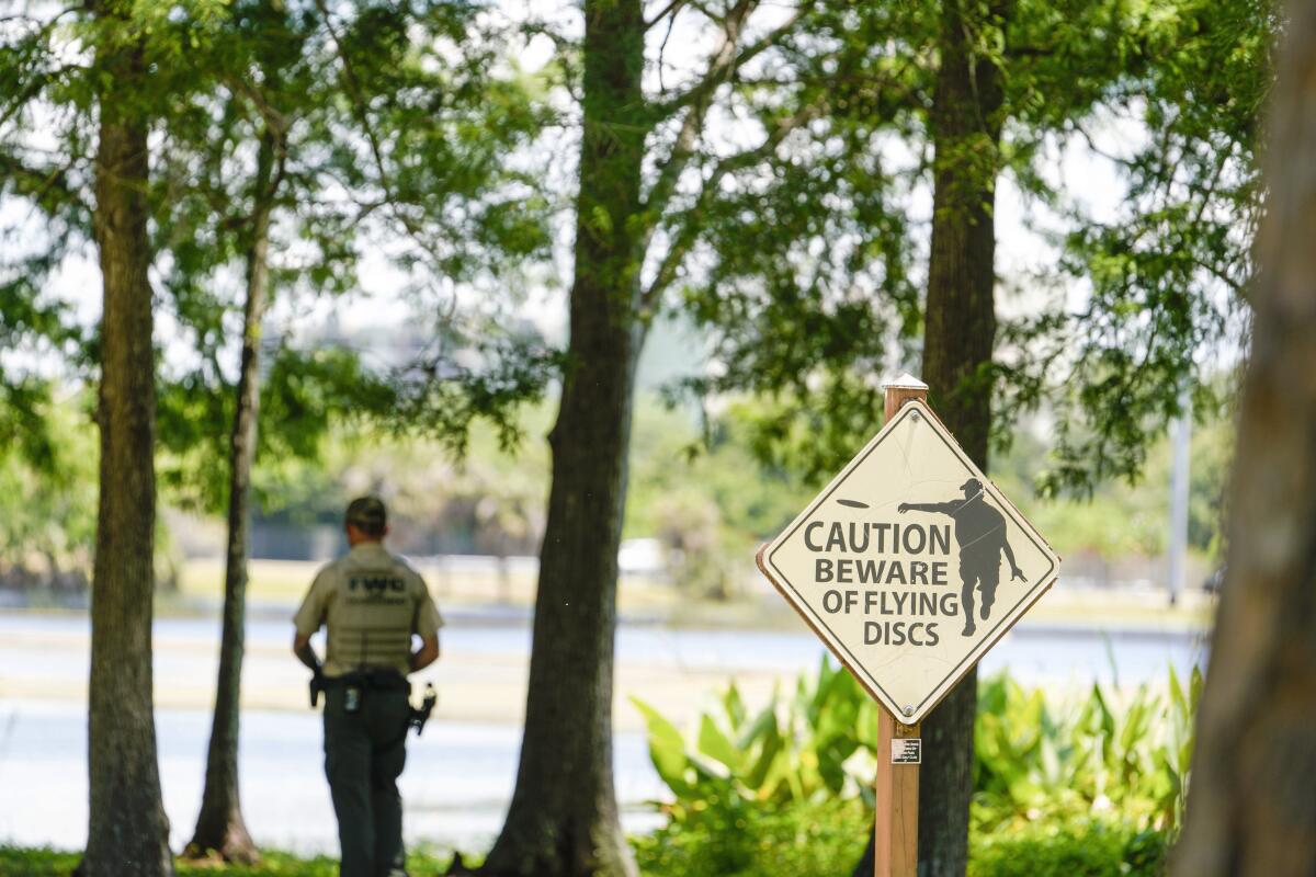 A Florida Fish and Wildlife Conservation Commission officers stands by a lake in John S. Taylor Park, where a man was found dead Tuesday, May 31, 2022, in Largo, Fla. Police believe he may have been wading into the water to retrieve lost flying discs. Investigators are still trying to determine whether he was bitten by an alligator. (Martha Asencio-Rhine/Tampa Bay Times via AP)