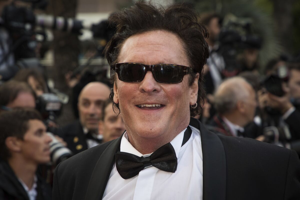 A smiling man wearing a tuxedo, bowtie and dark sunglasses