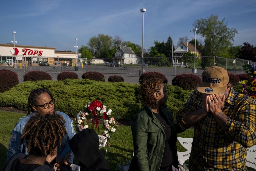 BUFFALO, NY - MAY 19: Curtis Hawkins, of Buffalo, right, covers his face with his hands, as he is comforted by Stephanie Dixon, and as his wife, Chantaye Hawkins looks on, near a memorial for the victims of a mass shooting at Tops Friendly Market at Jefferson Avenue and Riley Street on Thursday, May 19, 2022 in Buffalo, NY. The fatal shooting of 10 people at a grocery store in a historically Black neighborhood of Buffalo by a young white gunman is being investigated as a hate crime and an act of "racially motivated violent extremism," according to federal officials. (Kent Nishimura / Los Angeles Times)