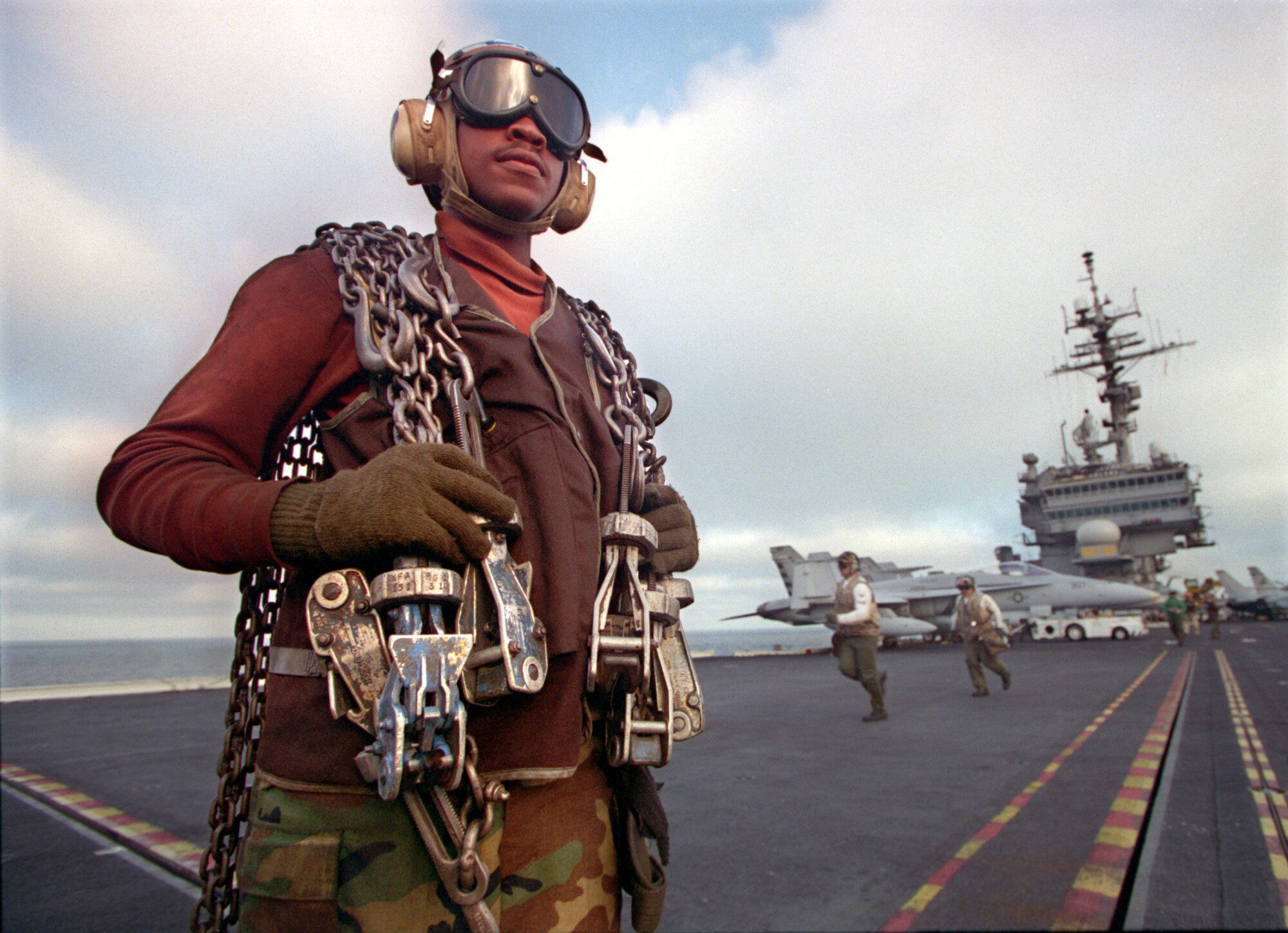 Airman Shawn Henderson waits to chain down an incoming fighter plane on the deck of the Kitty Hawk