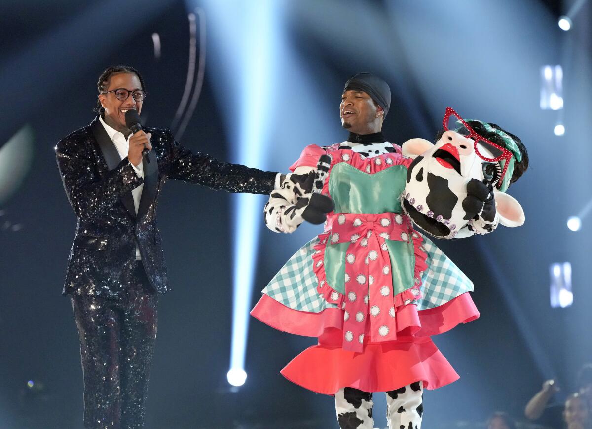 Nick Cannon in a sparkly black suit with Ne-Yo in a pink and turquoise dress, holding a fake cow head
