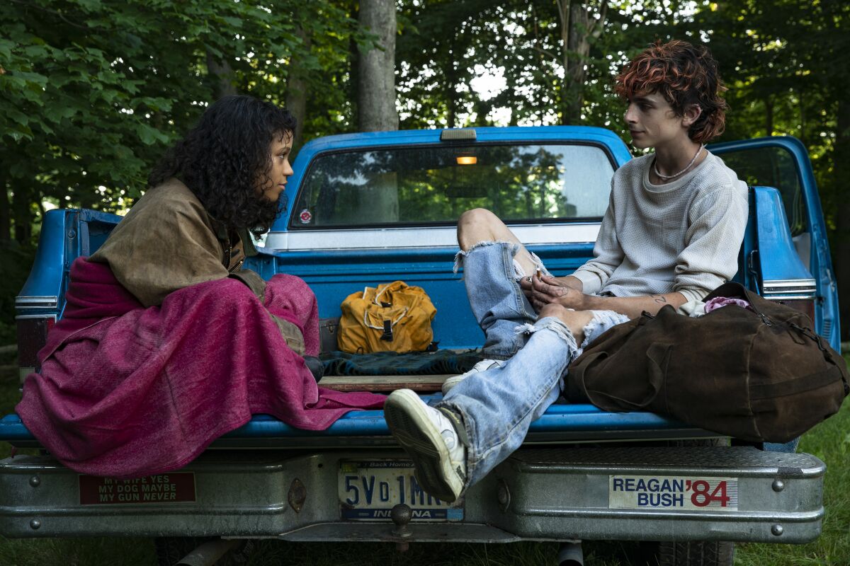 A young woman and young man sit in the bed of a pickup truck in a scene from "Bones and All."