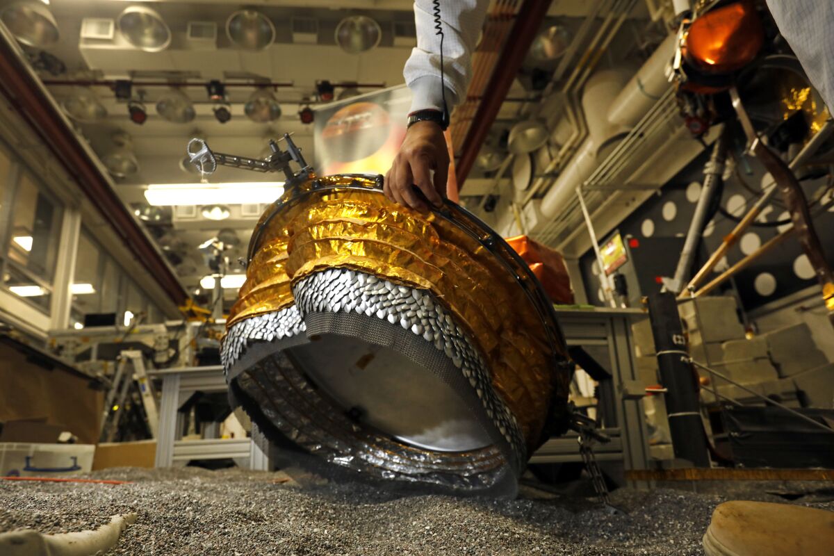 Pranay Mishra lifts up a model of InSight's wind and thermal shield.