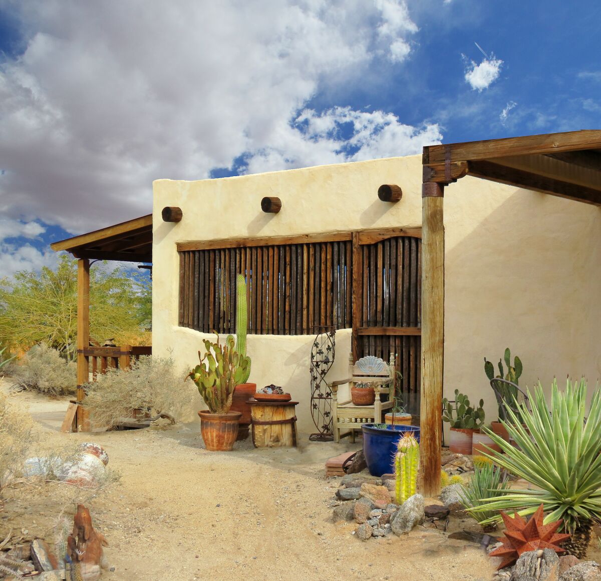 A Southwest home in the desert has handcrafted wooden posts and beams, and metal yard art mixed with yucca and cacti.