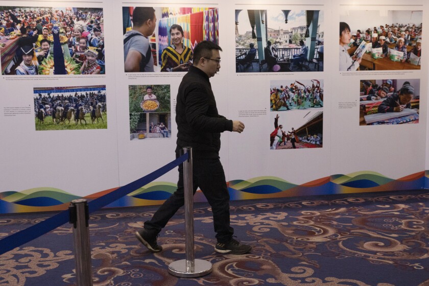 FILE - In this Dec. 11, 2019, file photo, a man walks past a display of photos from Xinjiang during a forum on human rights in Beijing. China has blasted a report from Human Rights Watch that accused it of constructing a surveillance state at home while seeking to silence critics abroad. (AP Photo/Ng Han Guan, File)