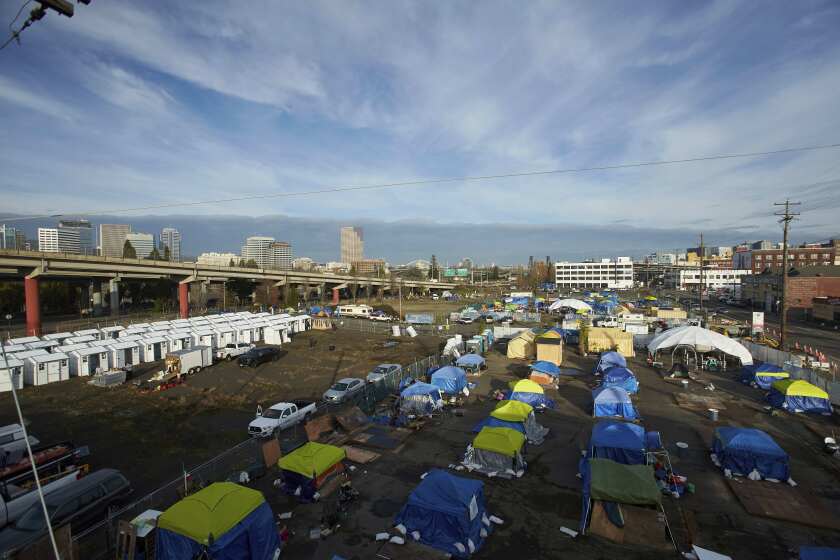 FILE - Homeless camps are seen in a vacant parking lot in Portland, Ore., Tuesday, Dec. 8, 2020. City Council members in Portland have voted to allocate $27 million of the city's budget to build a network of designated camping areas for homeless people. (AP Photo/Craig Mitchelldyer, File)