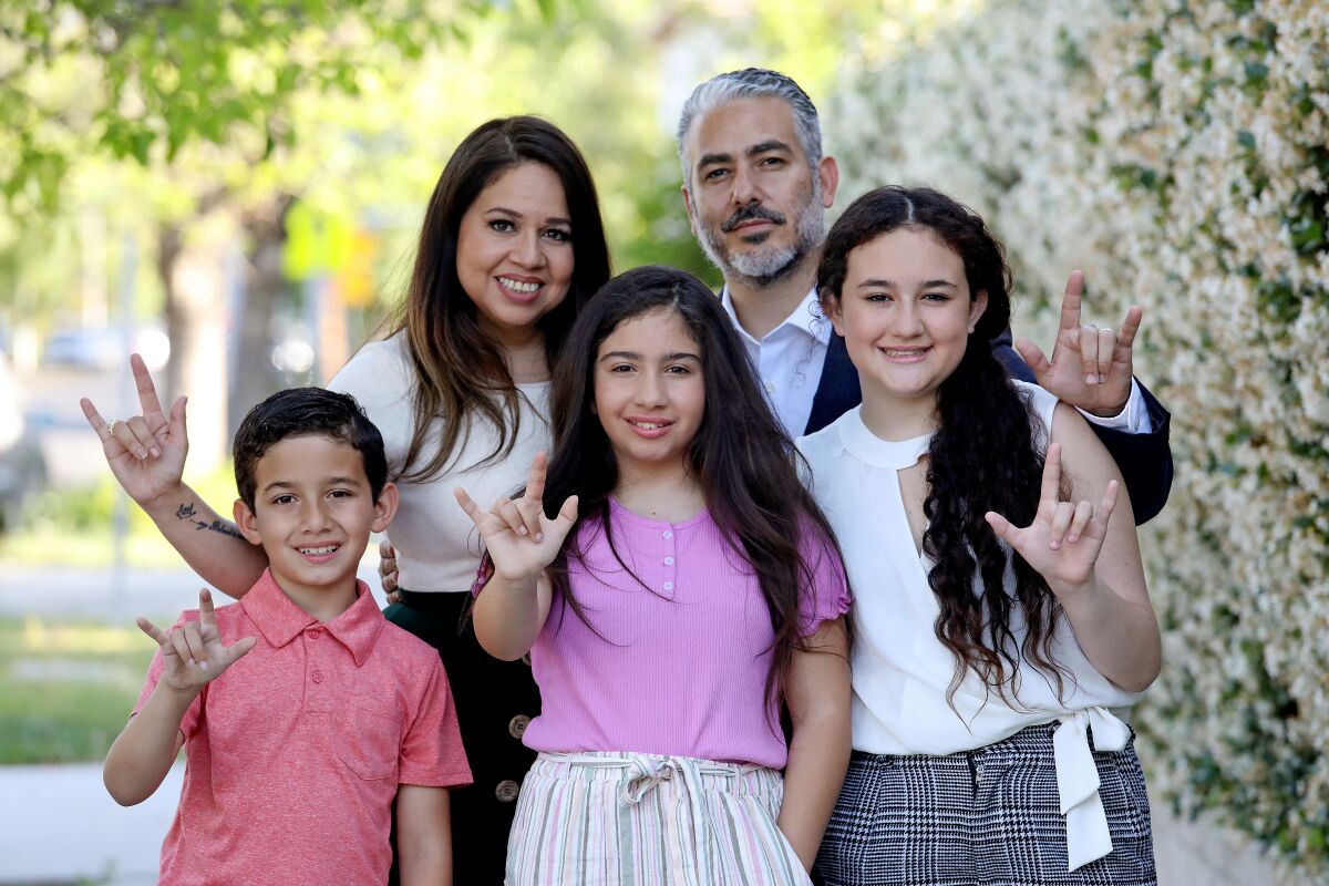 A family of five uses sign language to say "I love you" outside.
